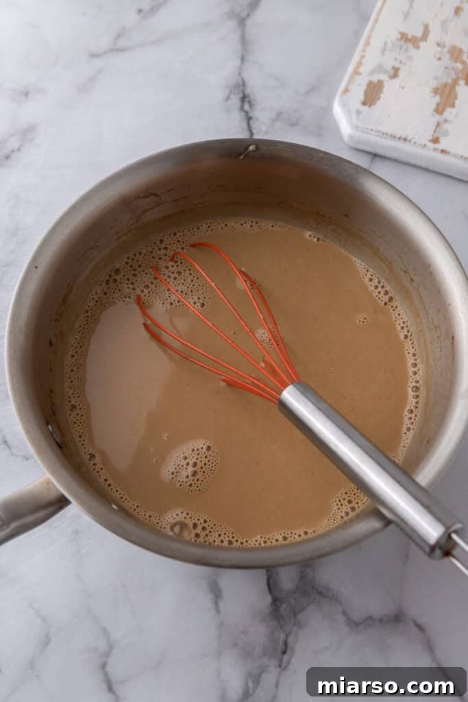 Tempered egg mixture being whisked back into the saucepan with cream