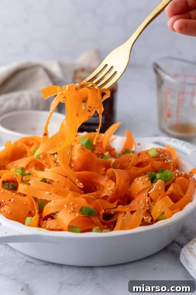 A fork picking up delicate carrot ribbons from a vibrant carrot ribbon salad, showcasing its fresh, crunchy texture.