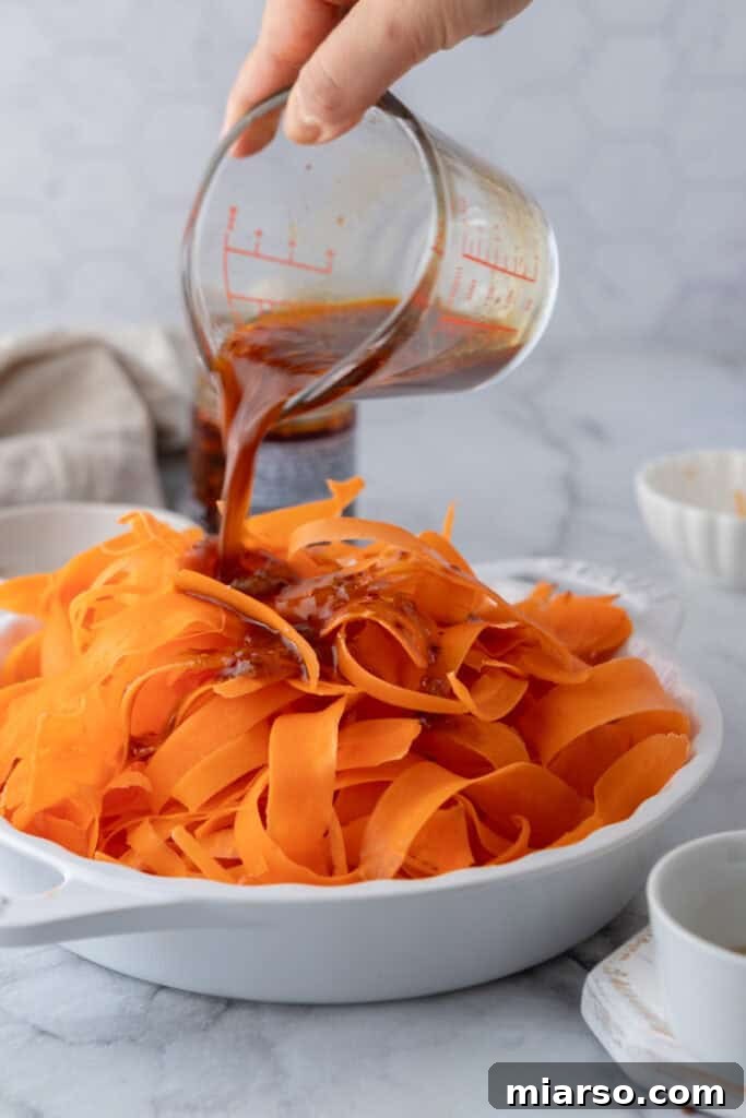 A stream of dressing being poured over a bowl of fresh carrot ribbons and green onions.