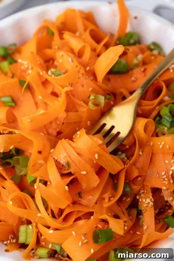 A hand reaching for a forkful of refreshing Carrot Ribbon Salad, emphasizing its inviting and ready-to-eat appeal.