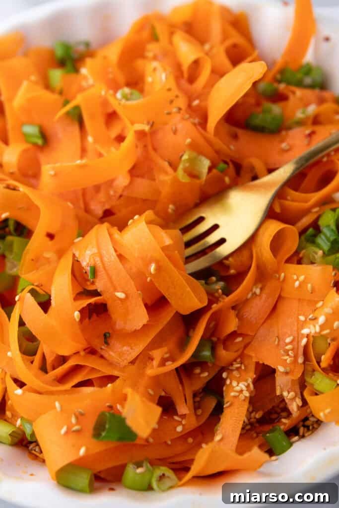 A fork lifts a generous serving of Carrot Ribbon Salad from a bowl, highlighting the thin, appealing slices and vibrant colors.