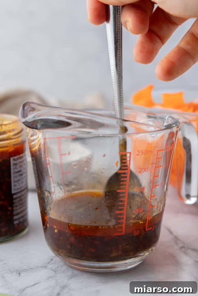 Close-up of chili crisp being added to a bowl of vibrant dressing ingredients.