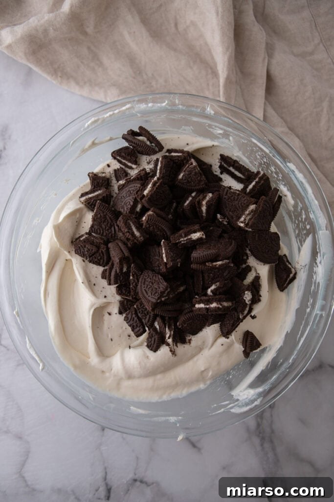Roughly chopped Oreos being added to the cheesecake filling
