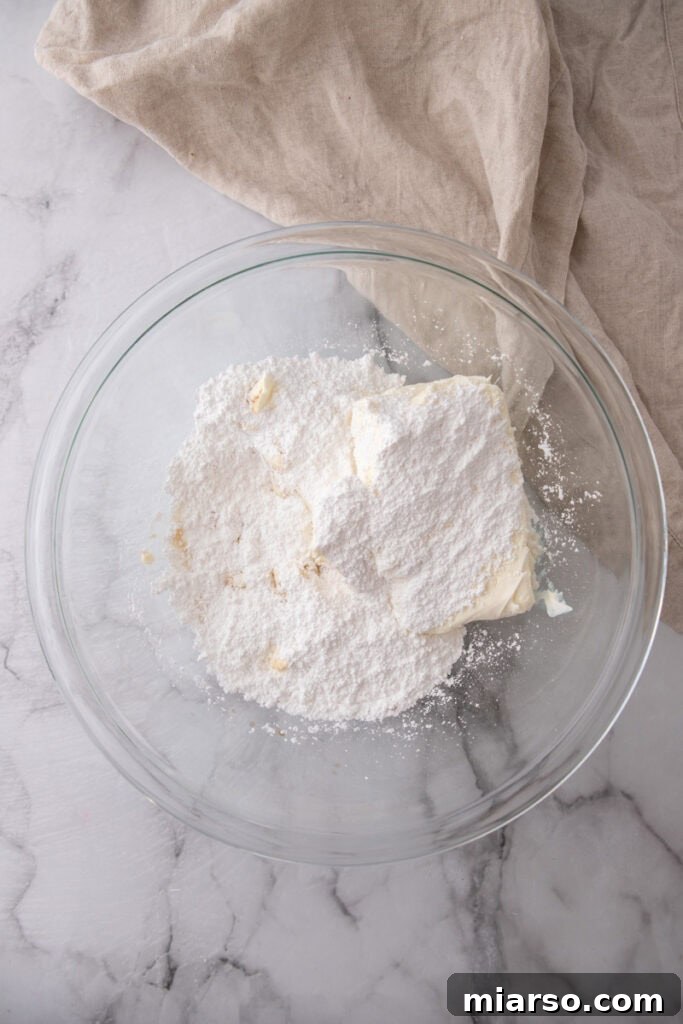 Cream cheese, powdered sugar, and vanilla extract being beaten in a mixing bowl
