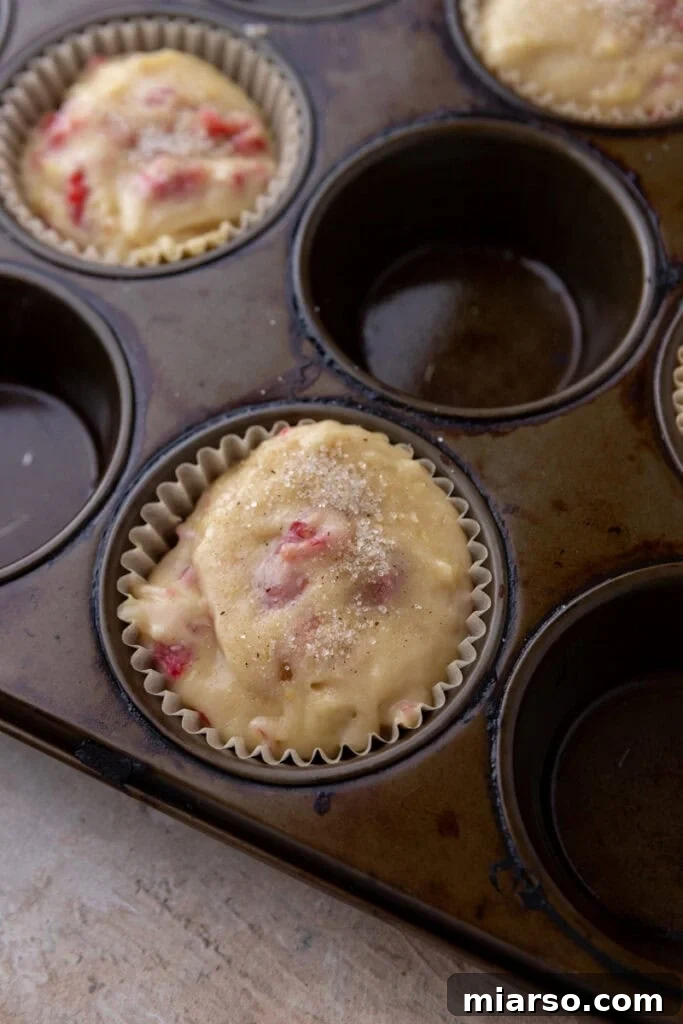 Muffin cups filled to the brim with batter and sprinkled with coarse sugar.