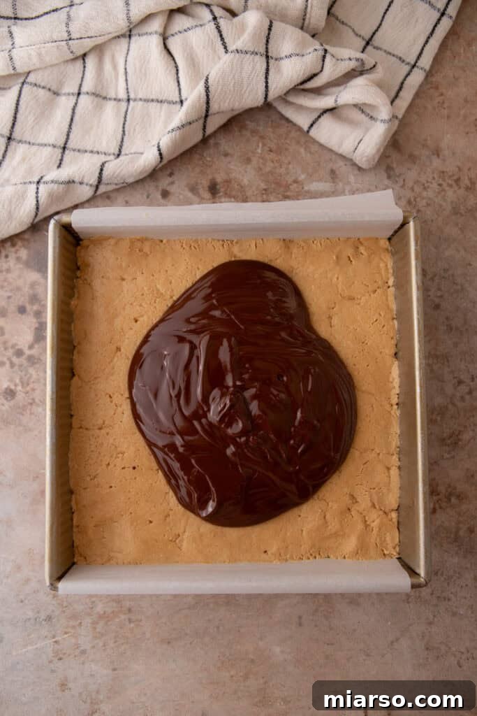Pouring melted chocolate over peanut butter layer