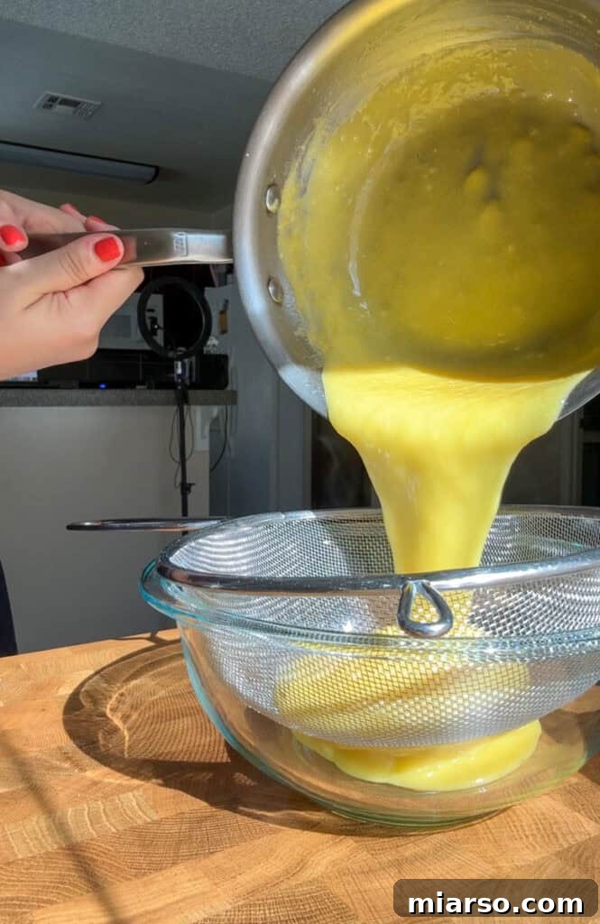 Straining yuzu curd through a fine-mesh sieve