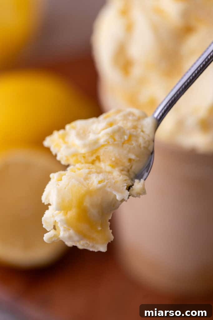 A spoon scooping creamy lemon custard ice cream, showcasing its smooth texture and optional lemon curd swirl.