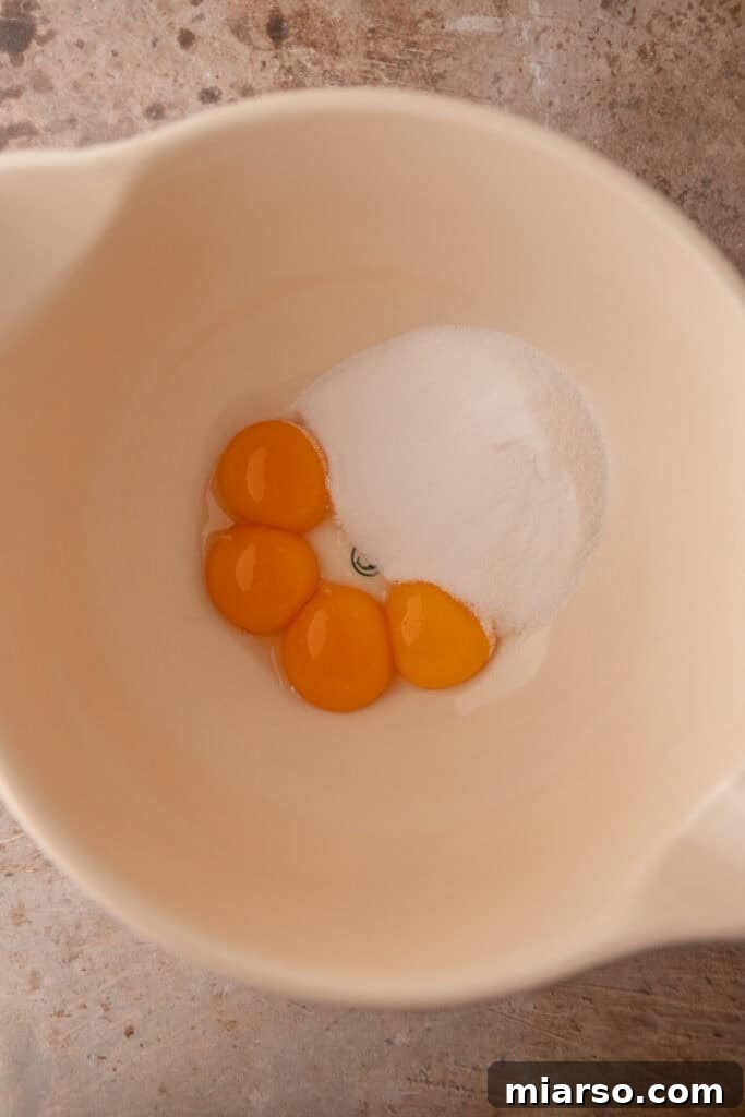Egg yolks, sugar, and salt being whisked in a bowl until pale and thick.