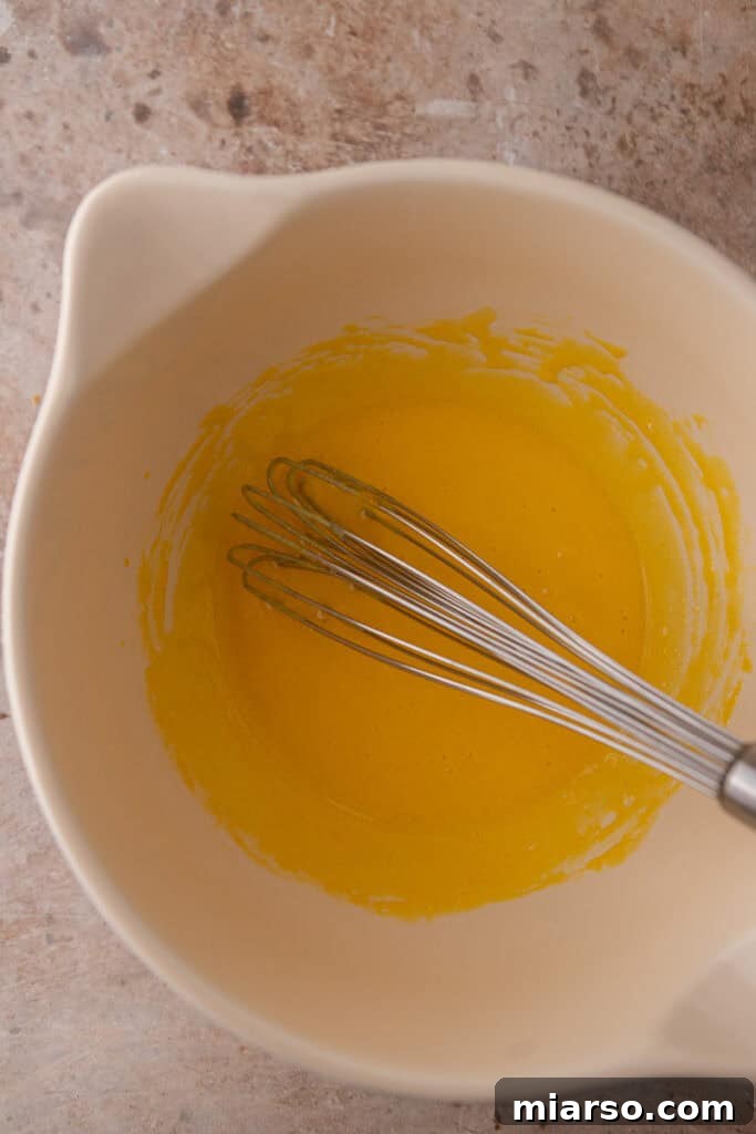 Tempering egg yolks by slowly adding warm milk mixture while whisking constantly.