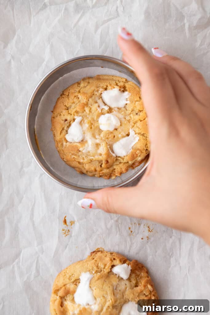 Another image of a hand swirling a cookie inside a cookie cutter to refine its shape and contain any oozed marshmallow.