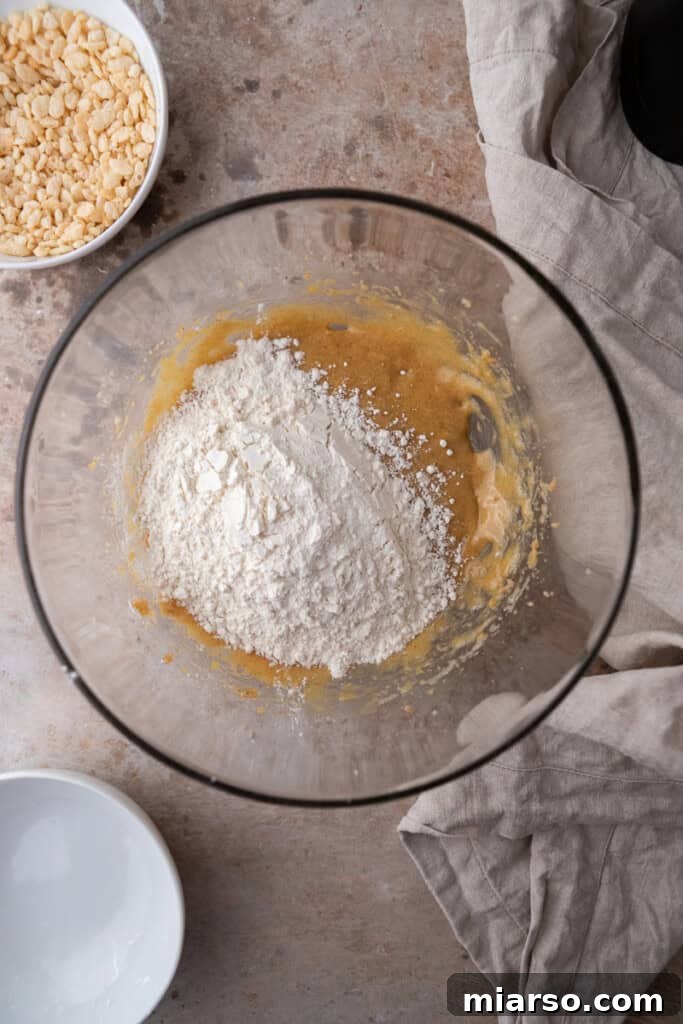 Wet ingredients in a bowl with dry flour mixture gradually being added, showing the transition to cookie dough.