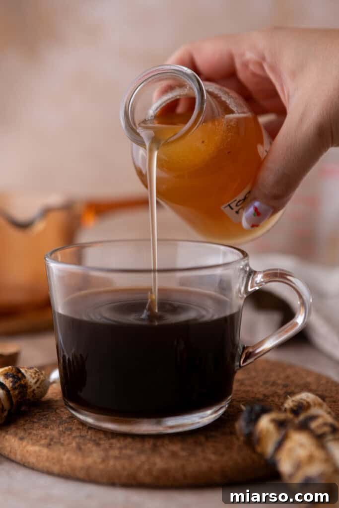 Freshly made toasted marshmallow syrup being poured into a cup of coffee, creating a luxurious swirl.