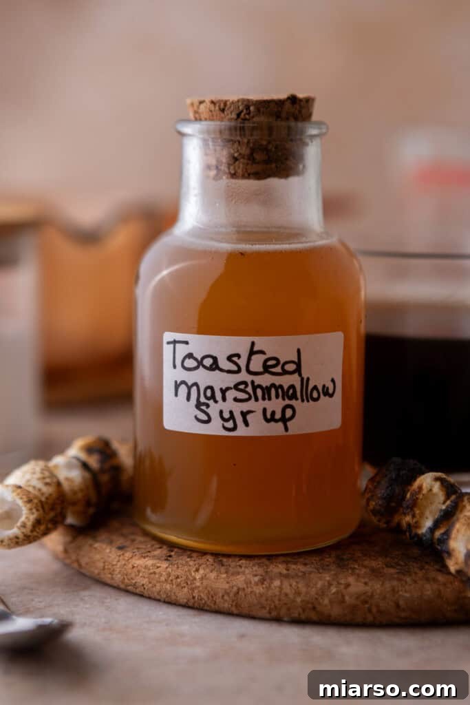 Homemade toasted marshmallow syrup being poured into a storage jar, ready for refrigeration.