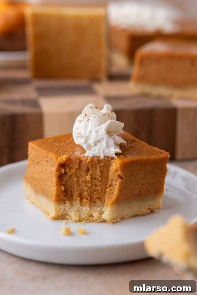 A sweet potato pie bar with a small bite removed from the corner, revealing the soft, creamy interior and the crispy shortbread crust texture.