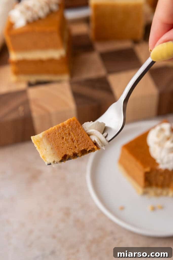 A sweet potato pie bar with a bite taken out, clearly showing the crisp shortbread crust and creamy filling, elegantly held on a fork.
