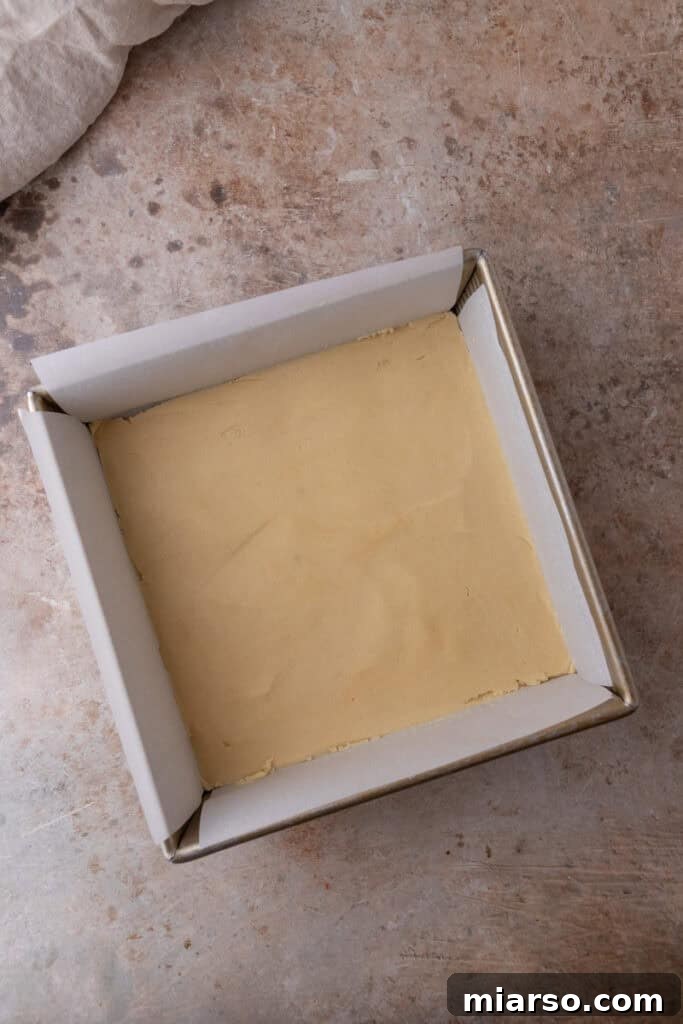 The unbaked shortbread crust expertly pressed into an even layer in the parchment-lined baking pan, prior to baking.