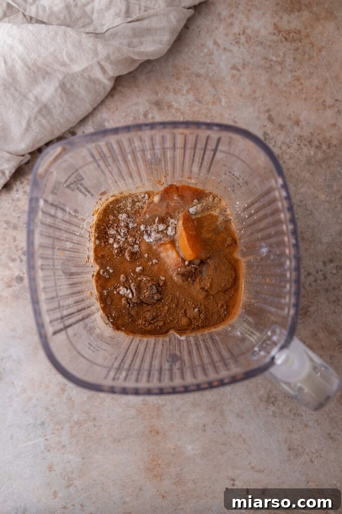 Cooked sweet potatoes and other vibrant filling ingredients, including evaporated milk and spices, placed in a blender, ready for blending.