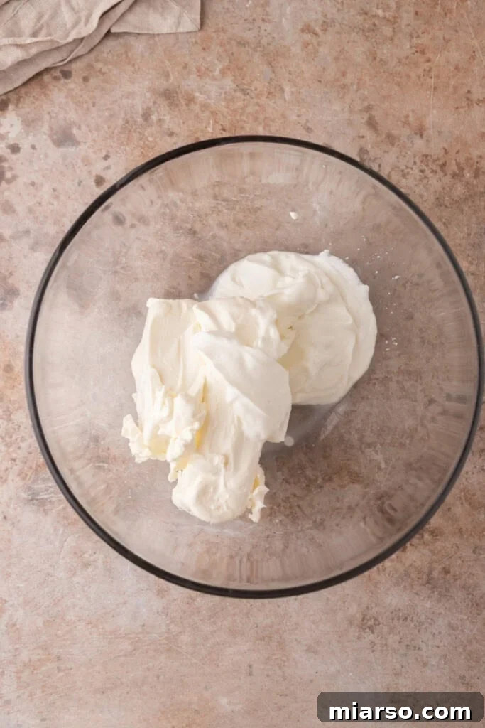Softened cream cheese and sour cream are beaten until smooth, forming the base of the cheesecake filling.