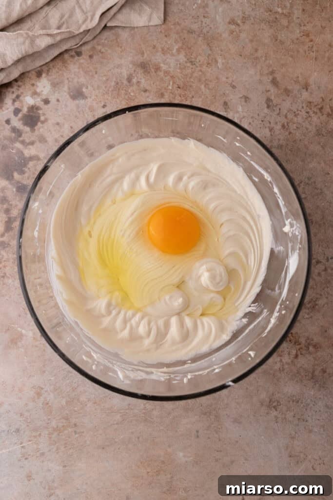Eggs are gently beaten into the cheesecake mixture on low speed, ensuring a smooth consistency without overmixing.