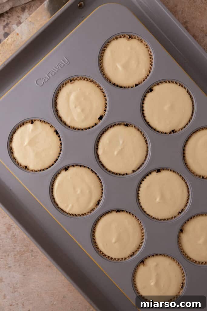Cheesecake filling carefully divided and poured over the graham cracker crusts in the muffin tin.