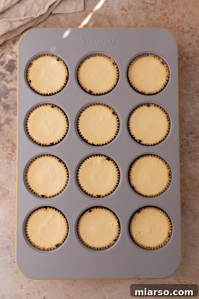 Baked mini cheesecakes in the muffin tin, cooled and ready for their final chilling before topping.
