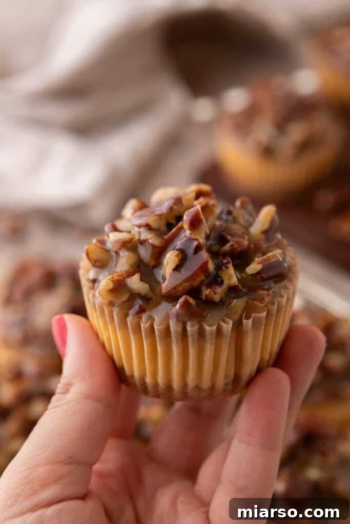 A hand holds up a single Mini Pecan Pie Cheesecake, showcasing its perfect individual portion and enticing layers.