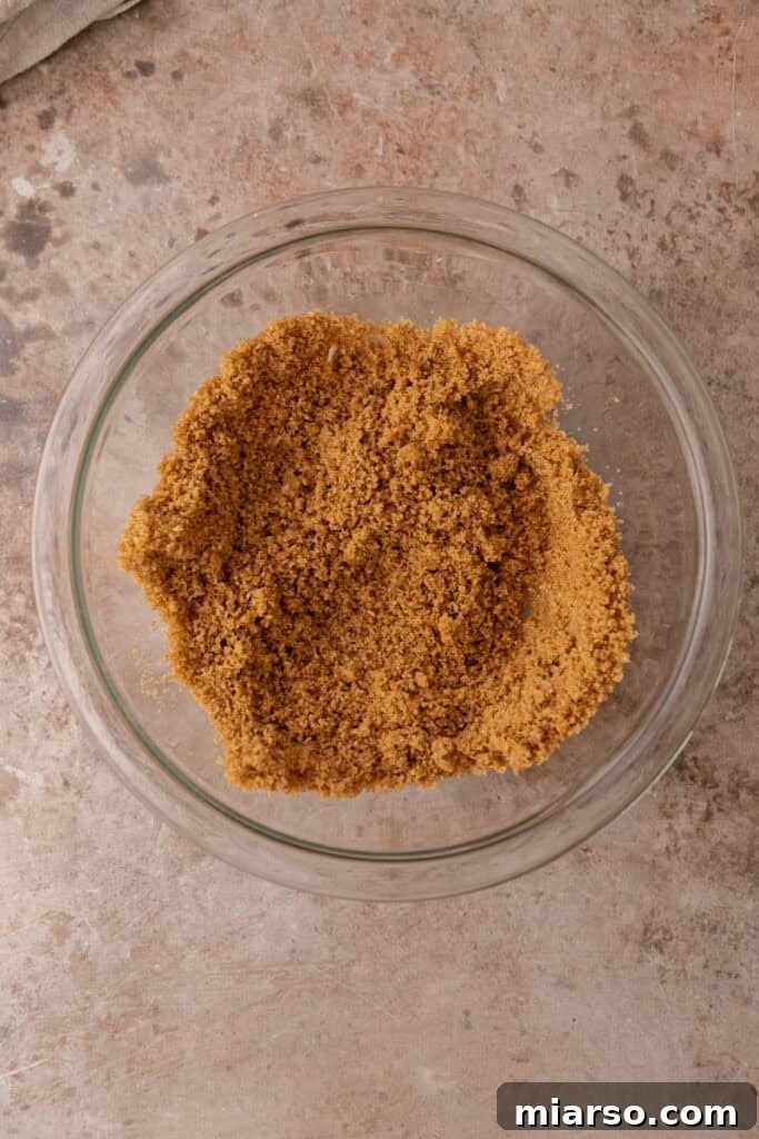 The graham cracker crust mixture is thoroughly combined, ready to be pressed into muffin liners for a firm base.
