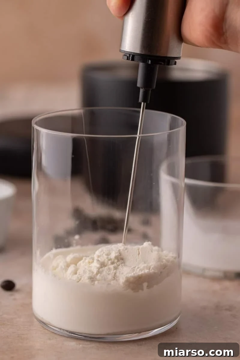 Starbucks Inspired High Protein Cold Foam 4 A handheld frother actively mixing cream and protein powder in a glass, illustrating the frothing process.