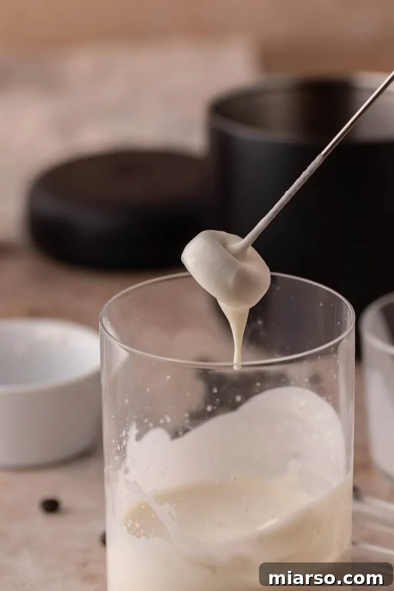 Starbucks Inspired High Protein Cold Foam 5 A thick, creamy cold foam is shown drizzling off a frother whisk, highlighting its rich and smooth texture.