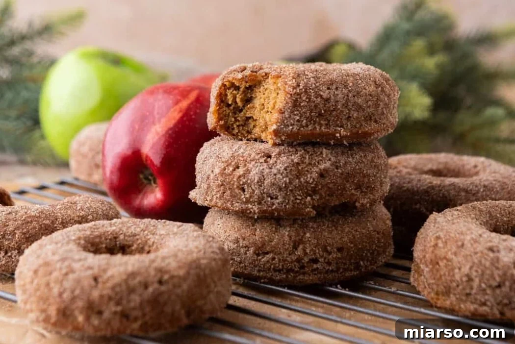 Fresh-baked apple cider donuts coated in cinnamon sugar, stacked with one donut showing a soft, fluffy inside.