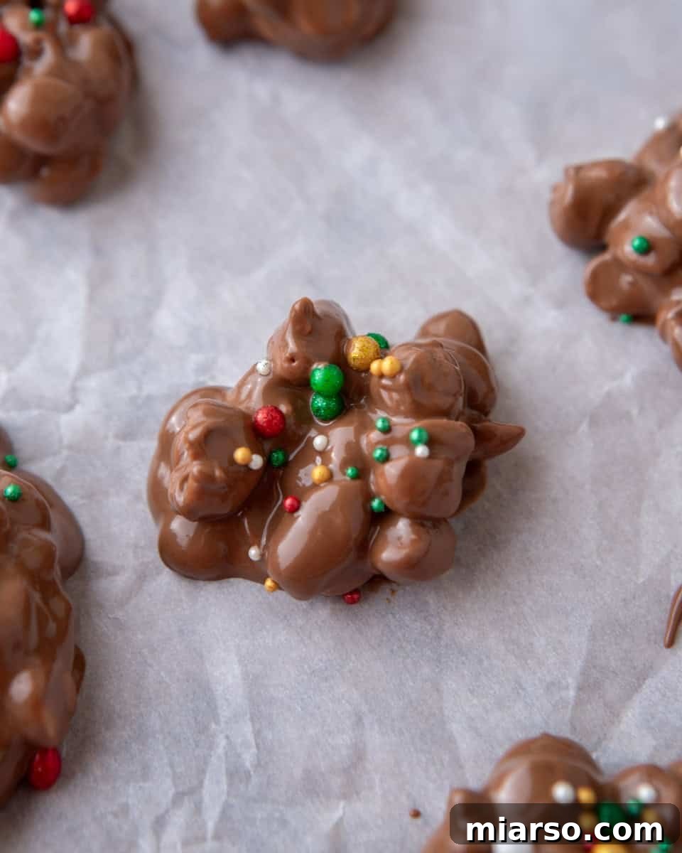Effortless Slow Cooker Chocolate Peanut Clusters 6 An unset crockpot candy cluster on parchment paper, freshly topped with an array of colorful Christmas sprinkles.