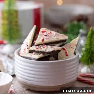 Peppermint bark pieces stacked in a white bowl, topped with crushed candy canes.