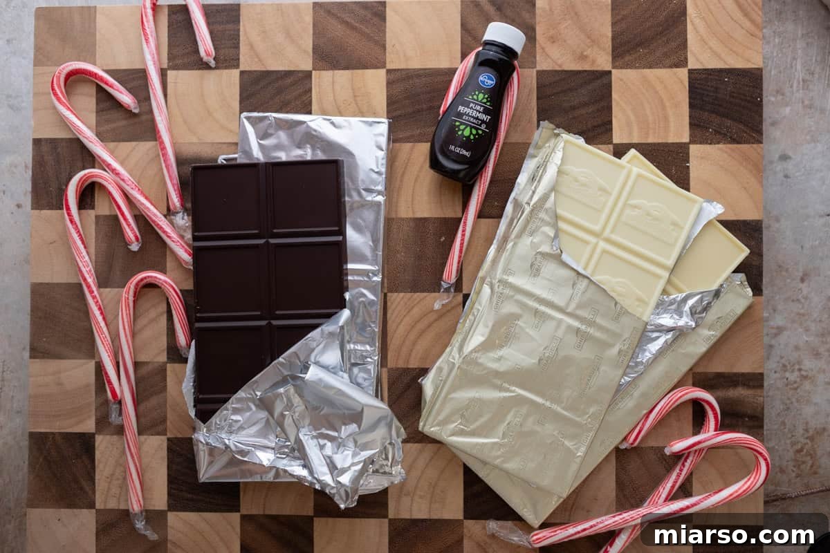 Dark chocolate bars, white chocolate bars, candy canes, and peppermint extract arranged on a rustic wooden board, ready for crafting peppermint bark.