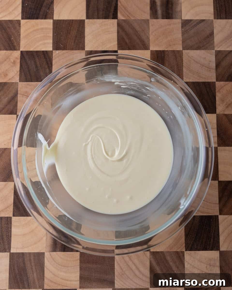Melted white chocolate swirled in a glass bowl on a wooden board, awaiting its addition to the dark chocolate layer.