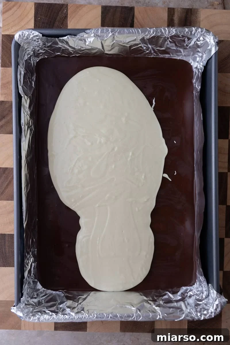 Melted white chocolate poured over a hardened dark chocolate layer in a foil-lined pan, creating the classic two-tone effect.