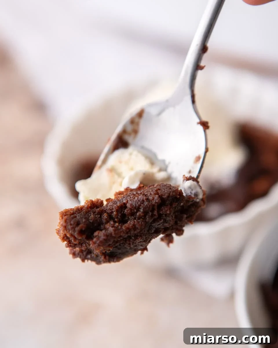 Ina Garten's Viral Brownie Pudding Sensation 10 A spoon laden with melted vanilla ice cream and a generous scoop of gooey chocolate brownie pudding, ready to be enjoyed.