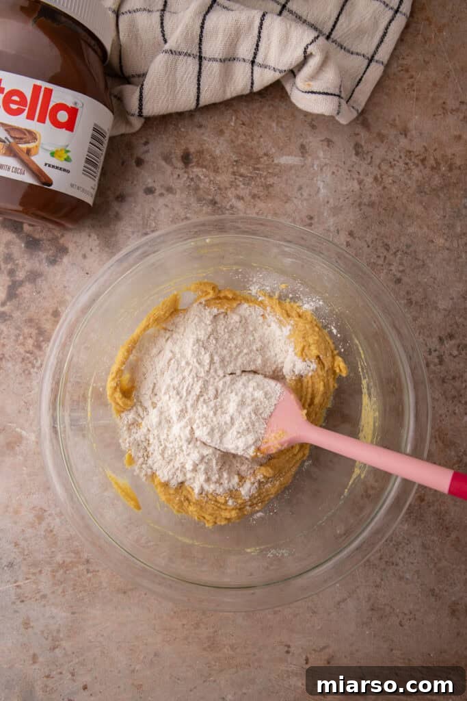 Dry ingredients added to wet cookie dough mixture in glass bowl