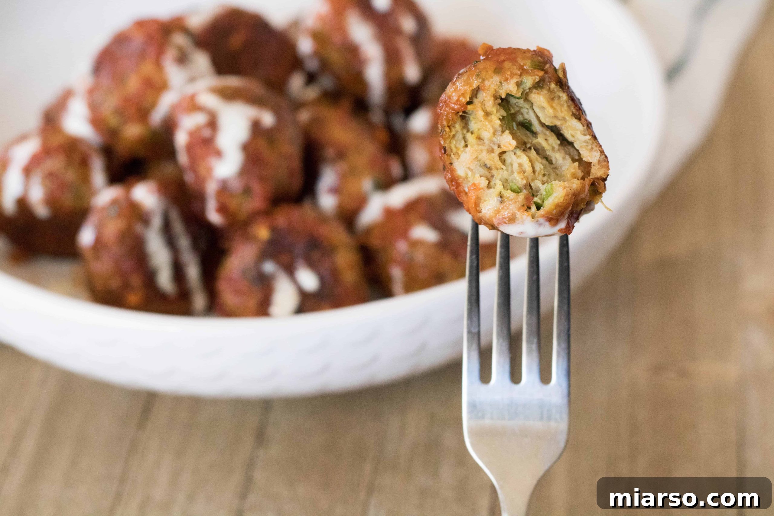 A plate of glazed Indian chicken meatballs with a vibrant, spicy sauce