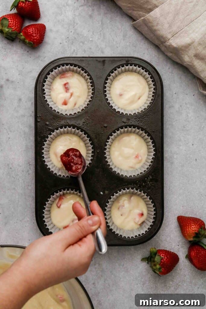 Placing a dollop of strawberry jam in the center of muffin batter