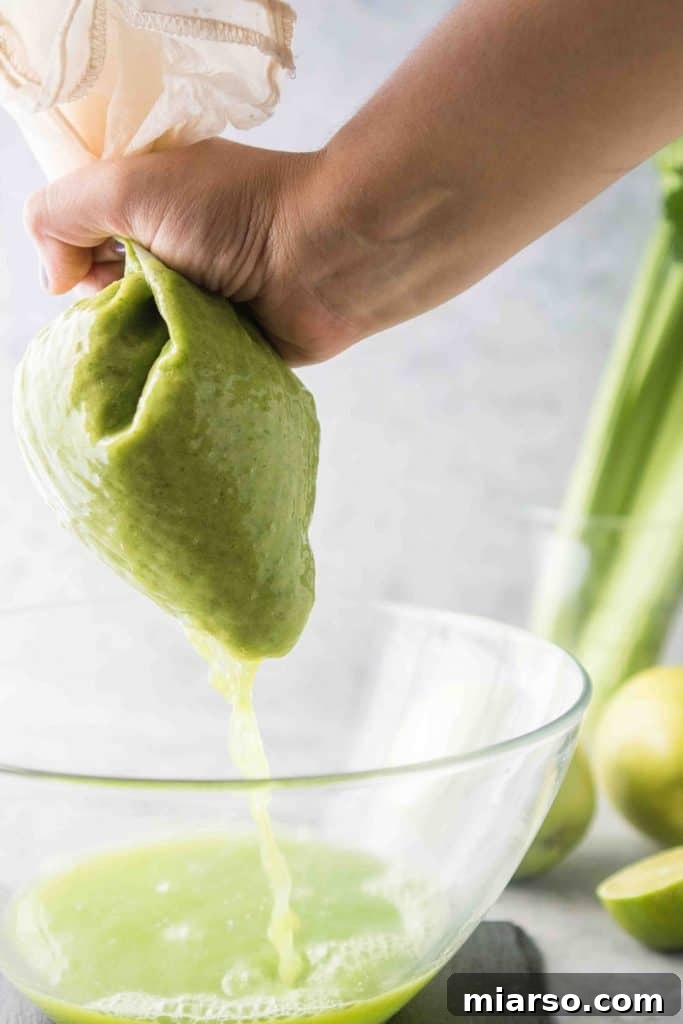 Hands squeezing green juice from a nut milk bag