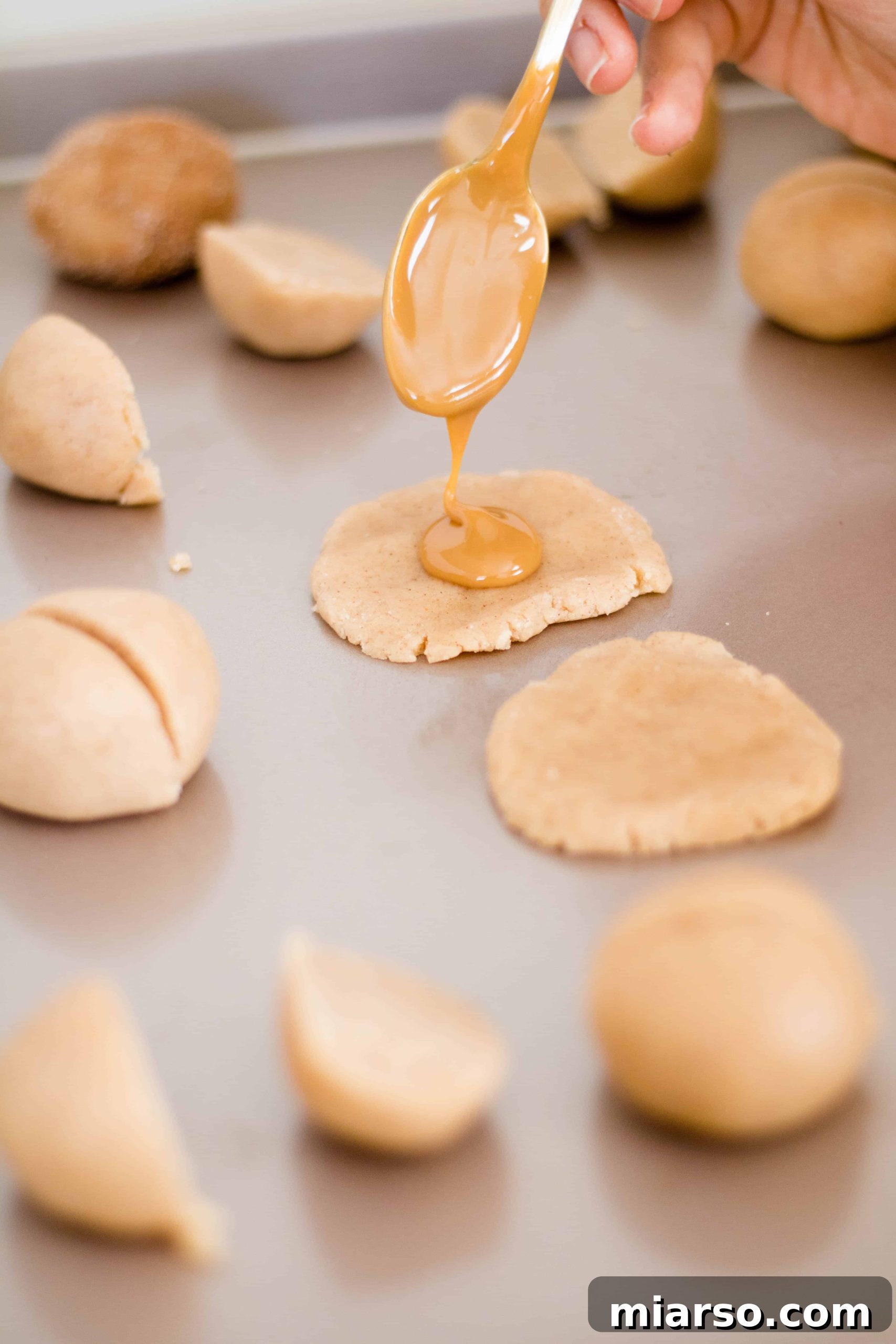 A delectable close-up of a Dulce de Leche stuffed Snickerdoodle Cookie, split in half to reveal the gooey, rich caramel filling. The cookie itself is soft and crinkled, dusted with cinnamon sugar, and the golden-brown dulce de leche glistens, promising a burst of sweet flavor. The texture is inviting, showcasing the perfect contrast between the chewy cookie and the smooth filling.