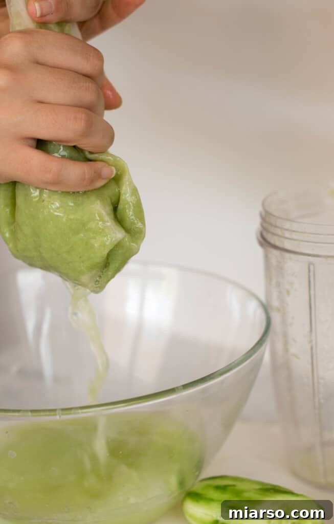 Hands squeezing grape juice from a nut milk bag into a bowl.