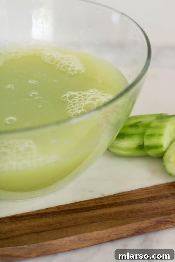 Close-up of strained grape and cucumber juice being collected in a bowl.