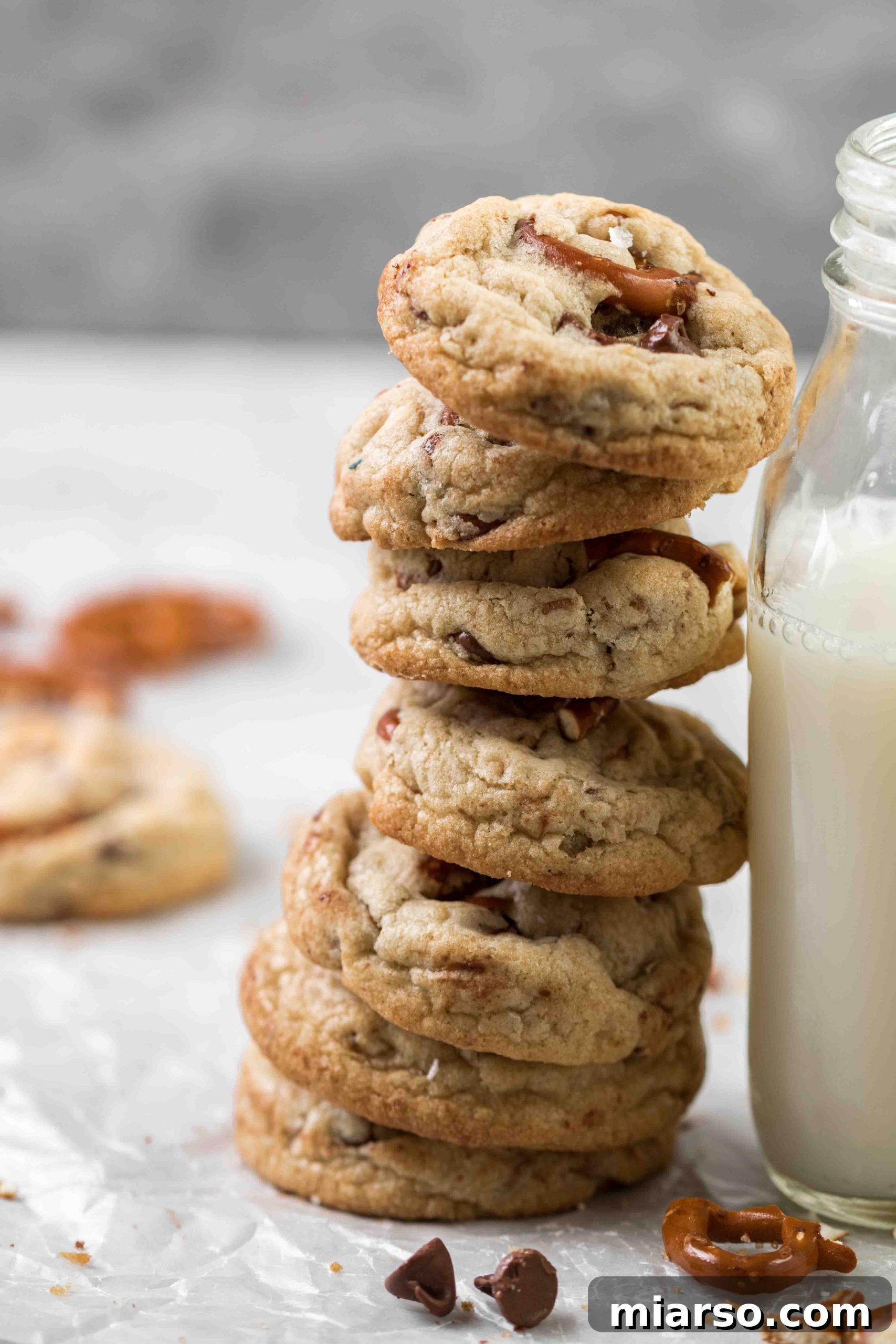 A close-up of a single warm pretzel chocolate chip cookie on a cooling rack, with visible melted chocolate and a sprinkle of sea salt.