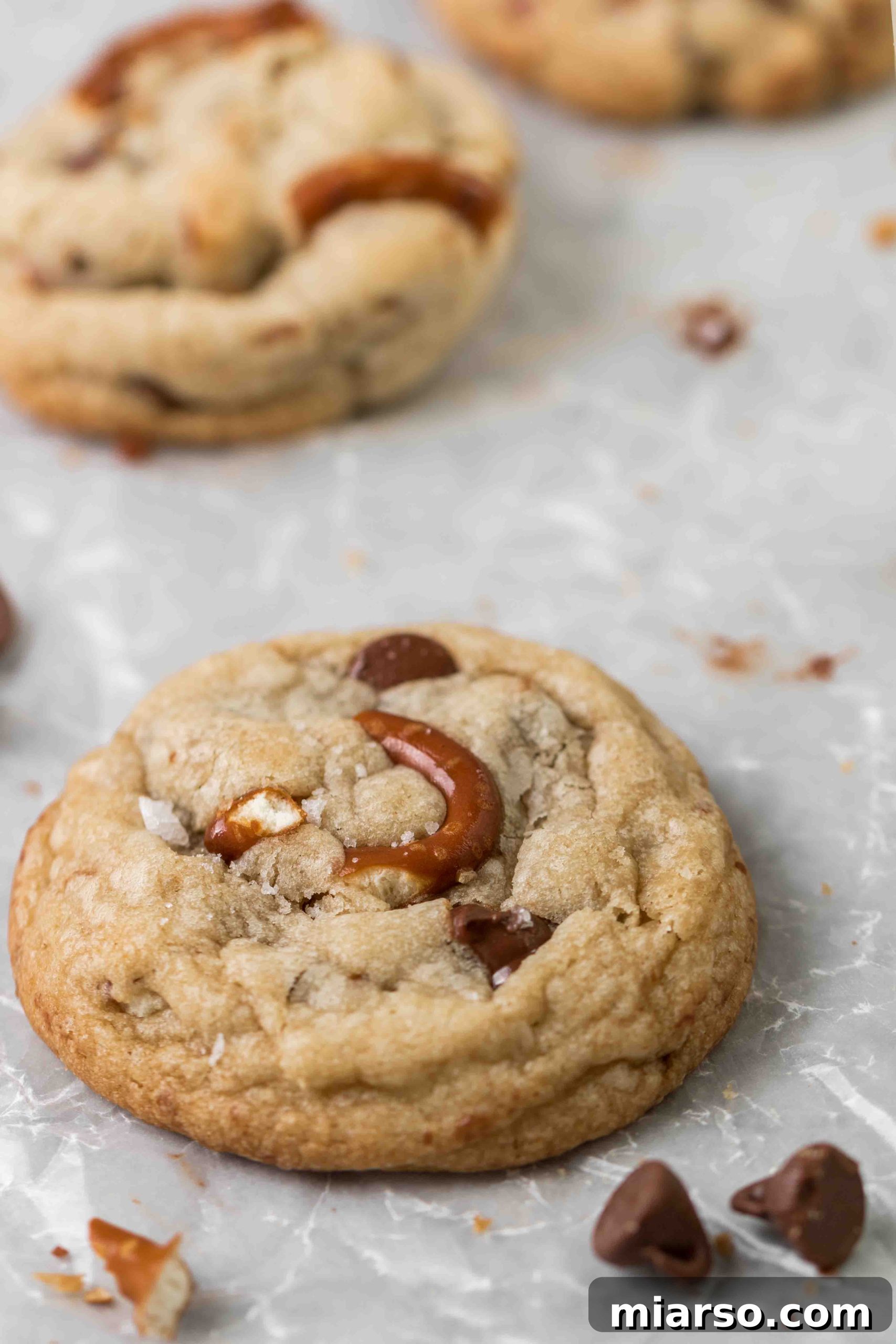 An overhead shot of several perfectly round, golden-brown pretzel chocolate chip cookies arranged on a light surface.