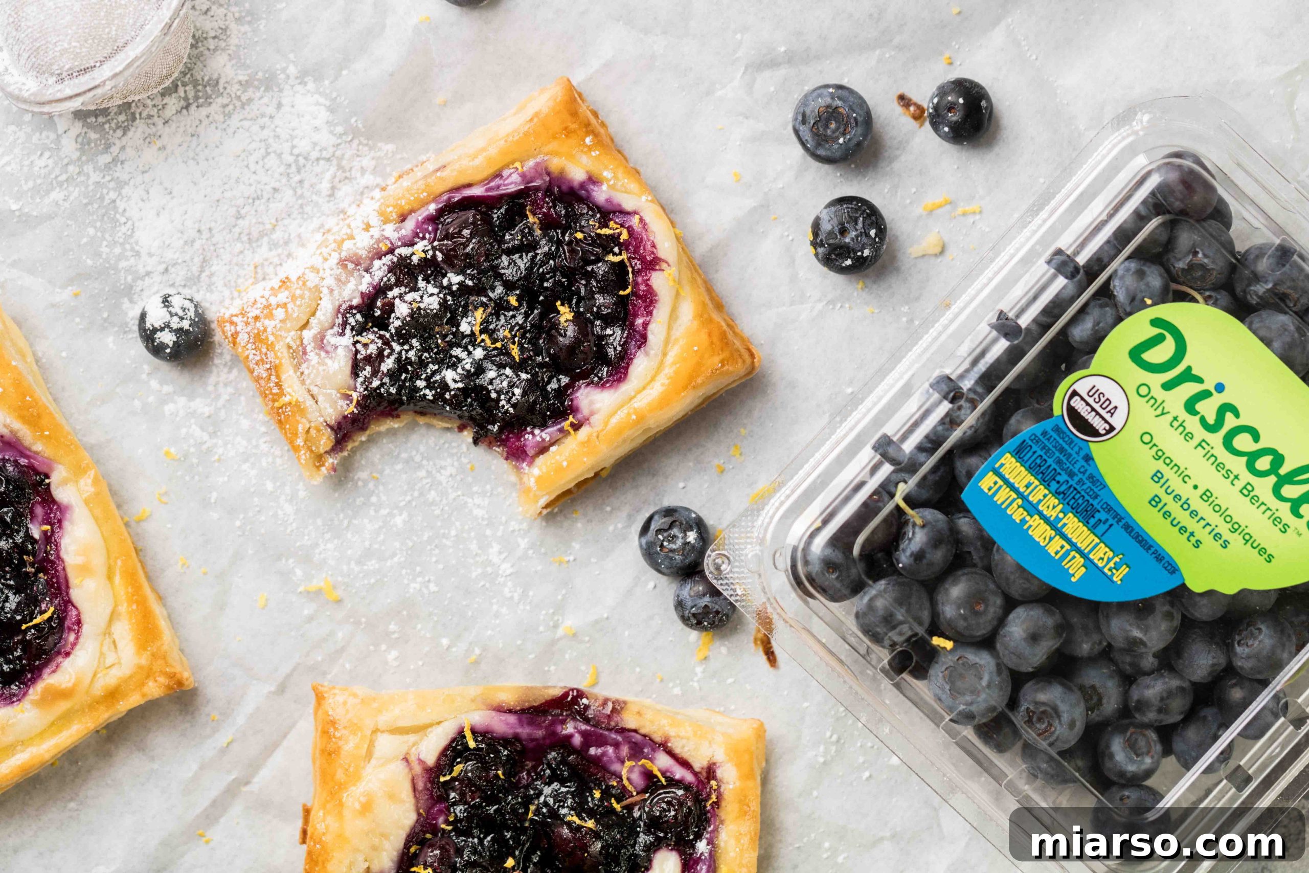 Flaky Blueberry Cheese Danish Made Easy 3 Close-up of a blueberry cheese danish on a white plate, showcasing its golden crust and fruit filling.