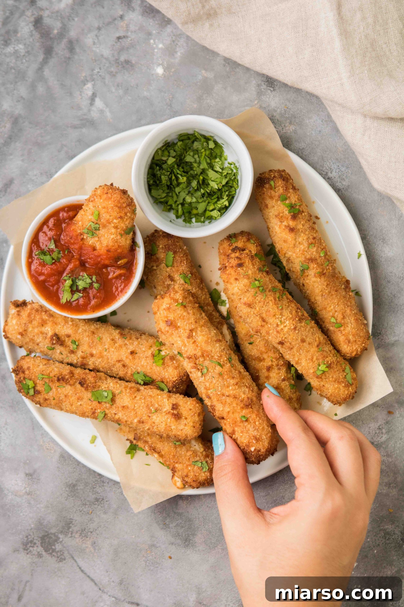 Airfryer'da Kusursuz Mozzarella Çubukları 3 Two air fryer mozzarella sticks on a plate with marinara sauce