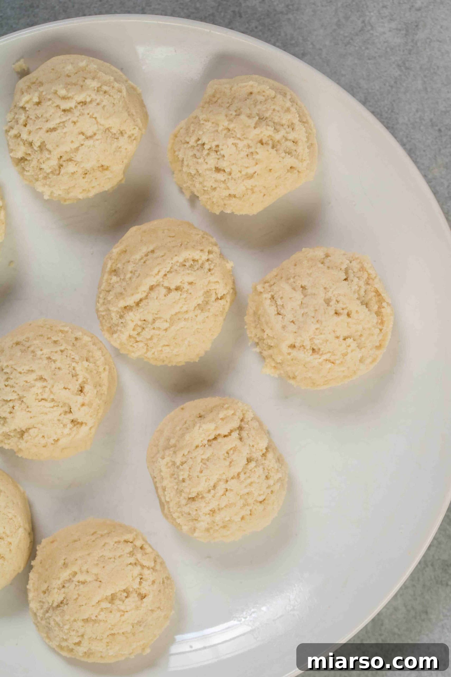 Rows of perfectly scooped vanilla sugar cookie dough balls, coated in sugar, ready for baking on a baking sheet.