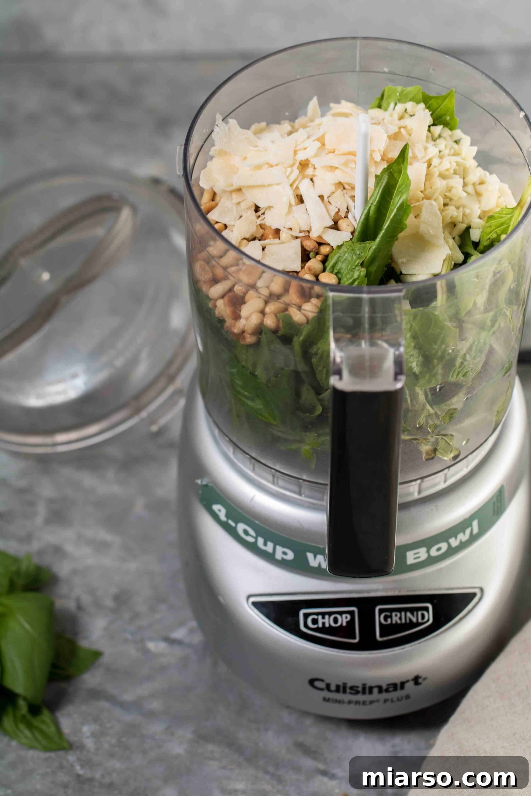 Effortless Homemade Pesto Perfection 4 Ingredients of the homemade pesto in a food processor, including basil, pine nuts, garlic, and cheese.